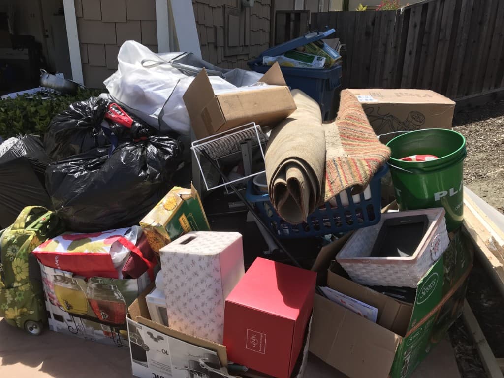Large estate cleanout with boxes, bags, rugs, and mixed household items piled outside