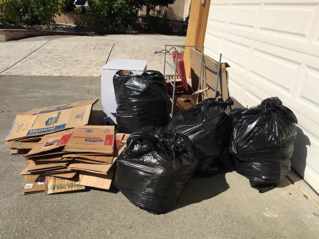 Bags, boxes, and furniture staged outside a garage for foreclosure cleanout